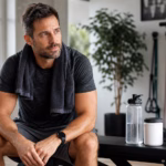 Man after a workout with water, resistance bands, and a neutral supplement container for blood flow support